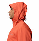 A man in profile wears Columbia’s Men’s Trailborne 2.5L Waterproof Shell Jacket in bright orange with hood up and drawstring; the Columbia logo is visible on the chest, set against a white background.