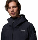 A man with wavy brown hair and light facial hair wears the black Columbia Mens Saudan Pro 3L Waterproof Shell Jacket with the hood up, looking at the camera against a plain white background.