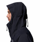 A person in profile wears a Columbia Mens Saudan Pro 3L Waterproof Shell Jacket with the hood up and adjustable drawstrings, set against a white background.