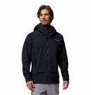 A man with light brown hair, facing forward with a neutral expression, is wearing a black Columbia Mens Saudan Pro 3L Waterproof Shell Jacket with a hood and front zipper, paired with light gray pants.
