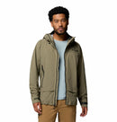 A man wearing a light olive green Columbia Mens Saudan Pro 3L Waterproof Shell Jacket over a light blue t-shirt and tan pants stands against a plain white background.