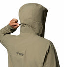 A person in a beige Columbia Mens Saudan Pro 3L Waterproof Shell Jacket adjusts the hood with the drawstring at the back. The Columbia logo on the upper back highlights its Omni-Tech Pro design for extreme conditions.