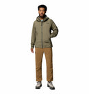 A man stands facing forward against a plain white background, wearing the Columbia Mens Saudan Pro 3L Waterproof Shell Jacket in olive green, paired with tan pants and gray hiking shoes.