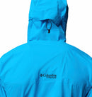 A person wearing a bright blue Columbia Mens Saudan Pro 3L Waterproof Shell Jacket is shown from the back with the hood up. The Columbia logo is visible in black on the upper back of this waterproof shell.