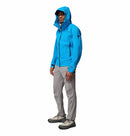 A man wears a Columbia Mens Saudan Pro 3L Waterproof Shell Jacket in bright blue, paired with light gray pants and gray hiking boots, standing against a plain white background.