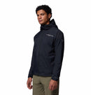A man stands slightly turned against a white background, wearing a black Columbia Mens Khyex Pro™ Wind Jacket with UPF 50 protection and olive-green pants.