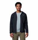 A person wearing a light blue shirt, olive green pants, and a black Columbia Mens Khyex Pro™ Wind Jacket with water and stain resistance stands against a plain white background.