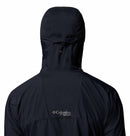 A person wears a black Columbia Mens Khyex Pro™ Wind Jacket, hood up, with the Columbia logo visible below the shoulders. The jacket offers water and stain resistance for enhanced protection.