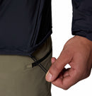 A close-up shows a person adjusting the drawcord on the hem of the Columbia Mens Khyex Pro™ Wind Jacket, pulling it tight with one hand. They are also wearing light khaki pants featuring a visible zippered pocket.