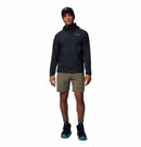 A man wearing the Columbia Mens Khyex Pro™ Wind Jacket, olive green shorts, black sneakers with blue soles, gray socks, and a black cap stands against a plain white background.