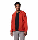 A man wearing the Columbia Mens Khyex Pro™ Wind Jacket in bright orange over a black shirt and light gray pants stands facing the camera against a plain white background.