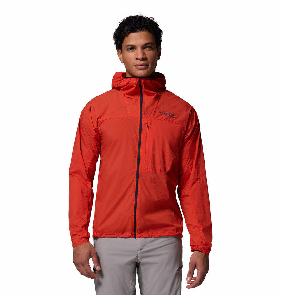 A person wearing the Columbia Mens Khyex Pro™ Wind Jacket in bright red with water and stain resistance, a front zipper, and gray pants stands facing forward against a plain white background.