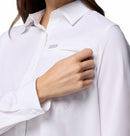 A woman in a Columbia Womens Silver Ridge Utility II Long-Sleeve Shirt touches the chest pocket with her right hand. The white moisture-wicking shirt has a small silver tag on the pocket. Her head is partially out of frame.