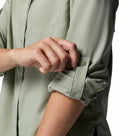 A woman rolls up the sleeve of a Columbia Womens Silver Ridge Utility II Long-Sleeve Shirt, securing it with a strap and button. This moisture-wicking trail shirt keeps you cool and comfortable on every adventure.