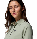 A woman with long brown hair wears the Columbia Womens Silver Ridge Utility II Long-Sleeve Shirt in light green with UPF 50 sun protection, standing against a white background and smiling gently while looking to the side.