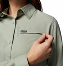 A person in a light green Columbia Womens Silver Ridge Utility II Long-Sleeve Shirt unzips the chest pocket, showing only their upper body and hand against a white background. The shirt offers moisture-wicking fabric and UPF 50 sun protection.