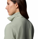 A woman with straight brown hair is shown from the side and back, wearing a light green Columbia Womens Silver Ridge Utility II Long-Sleeve Shirt with UPF 50 sun protection and a turned-up collar, set against a plain white background.