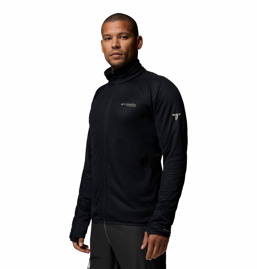 A man wears a black Columbia Mens Summit Step™ Full Zip Technical Fleece, standing slightly turned and looking at the camera with a neutral expression. The plain white background highlights the jacket’s lightweight design.