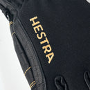 A close-up of the Army Leather GORE-TEX Short Glove displays a black ski glove with yellow stitching and the Hestra logo embroidered in yellow on the back, emphasizing its exceptional performance as a waterproof winter glove.