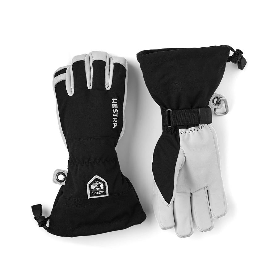 A pair of Hestra Army Leather Heli Ski Gloves in black and white, featuring extended cuffs, an adjustable strap, and drawstring closures for a secure fit, with the Hestra brand name on one glove and a small wrist patch.