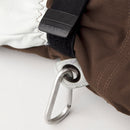 Close-up of a brown and white Hestra Army Leather Heli Ski Glove, showing a black strap with the HESTRA label and a metal carabiner attached to a fabric loop on the glove.