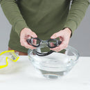 Person cleaning goggles with a clear bowl on a white surface
