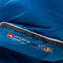 A close-up of a blue The North Face Cat’s Meow Sleeping Bag (-7°C) shows its label, indicating it is designed for backpacking and rated for -7°C (20°F). The sleeping bag is partially unzipped, revealing the interior made with recycled synthetic insulation.