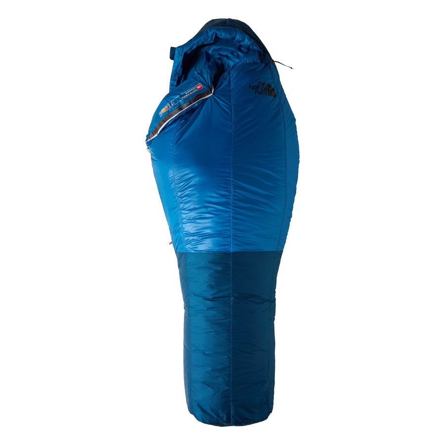A blue Cat’s Meow Sleeping Bag (-7°C) by The North Face, featuring a shiny insulated shell with recycled synthetic insulation, a hood, and a zippered side—specifically designed for cold weather camping—with The North Face logo displayed on the upper section.