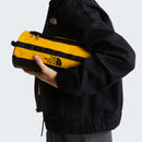 A person in a black The North Face jacket holds a yellow and black Base Camp Travel Washbag - Large by The North Face—one of the brand’s many durable travel accessories—against a plain background.