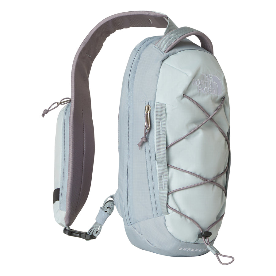 The North Face Borealis Sling Bag in light gray and pale blue is crafted from recycled nylon and designed for everyday adventures, featuring a padded strap for comfort, a zippered pocket, a front bungee cord, and the brand’s signature logo embossed on the top front—making it an ideal compact sling bag.