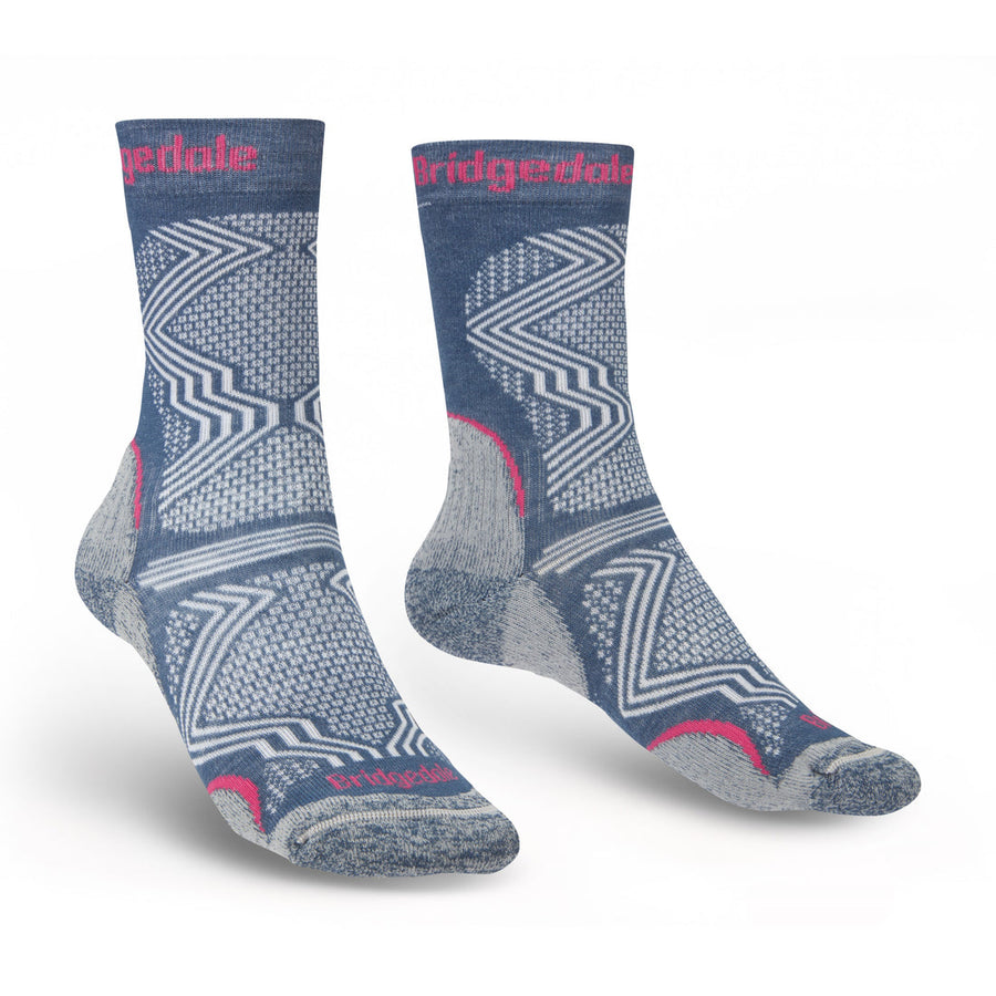 The Bridgedale Womens Hike Ultra Light T2 Coolmax Performance Boot Sock is a blue and gray hiking sock with pink details, geometric patterns, reinforced heel and toe, breathable fabric, and the Bridgedale logo in pink near the top.
