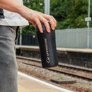 A person holding a Lifeventure One-Touch Thermal Mug in black, featuring a one-touch lid, stands on a train platform with tracks and trees in the background.