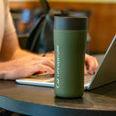 A person types on a laptop at a table with a Lifeventure One-Touch Thermal Mug featuring a One-Touch Lid in the foreground.