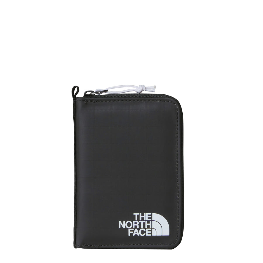 The North Face Base Camp Voyager Wallet is a sleek black zippered travel wallet made from recycled fabric, featuring the brands white logo at the bottom right corner and a convenient pocket for a tracking tag.