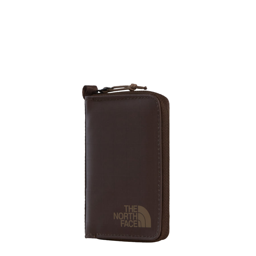 The Base Camp Voyager Wallet from The North Face is a brown zippered wallet made from recycled fabric, featuring the brand’s gold logo on the front. Photographed against a plain white background, this travel wallet combines eco-friendly design with style for your everyday adventures.