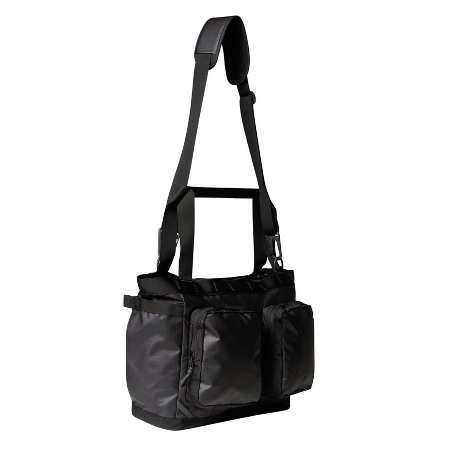 A black Base Camp Voyager Tote Bag from The North Face—featuring a wide adjustable strap, multiple compartments, and zippered front pockets, all crafted from recycled durable fabric—is displayed against a white background.