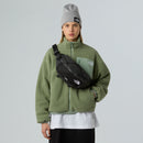 A person wearing a gray beanie, a green fleece jacket, and a white shirt—all by The North Face—stands against a plain light gray background, carrying the Terra 6-Litre Bum Bag from The North Face and ready to bring their hiking essentials in style.