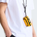 A person wearing a white t-shirt and black pants with hands in their pockets carries The North Face Base Camp Mini Duffel, featuring black accents and hanging from a black-and-white cord around their neck.