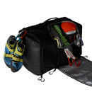 A black Great Outdoors Base Camp Boot Bag, engineered with the versatility of a ski boot bag, showcases climbing shoes, rope, an orange helmet, carabiners, and additional climbing gear organized inside and attached to the exterior. The open side compartment neatly displays all the essential items.