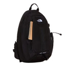 A black North Face Hot Shot Sling Bag featuring a spiral notebook partially tucked into the front pocket and a mesh water bottle holder on the side, offering versatile storage reminiscent of modular sling bags and compact crossbody styles.