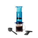 Blue AeroPress coffee maker with a glass mug of coffee and accessories on a white background