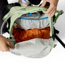 The open green Rab Airox ND22L Day Pack is shown from above, revealing an orange inner compartment, a white interior pocket, and a hydration bladder with an attached tube. Two hands hold the pack open; this women’s hiking backpack from Rab also features a ventilated AEROFIT back system for enhanced comfort.