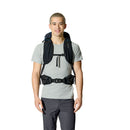 A person wearing a light gray T-shirt and dark pants is smiling at the camera, showcasing the Rab Airox 30L Hiking Pack—a ventilated hiking backpack equipped with Rab’s advanced AEROFIT back system—its multiple straps visible as they stand against a white background.
