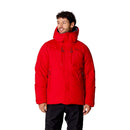A person wearing the Rab Batura Jacket—a bright red, waterproof, and puffy down jacket filled with 800FP European goose down—stands facing forward, smiling with hands relaxed by their sides. Paired with black pants, this insulated jacket is ideal for cold weather and high-altitude expeditions.