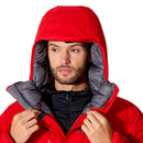A man wearing a Rab Batura Jacket—with the red hood up and its gray inner lining visible—looks off to the side while holding the collar with both hands, highlighting the warmth and protection of this 800FP European goose down, waterproof jacket designed for high-altitude expeditions.