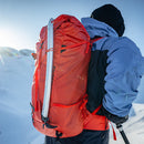 Person with a red backpack and blue jacket standing on a snowy mountain