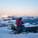 Person on a snowmobile in a snowy mountain landscape with a red backpack