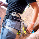 Person wearing a climbing harness with ropes on a rock climbing wall.