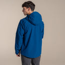 A man wearing the Craghoppers Mens Ponsa Waterproof Jacket in blue and dark pants stands facing away, looking to the side, against a plain beige background.