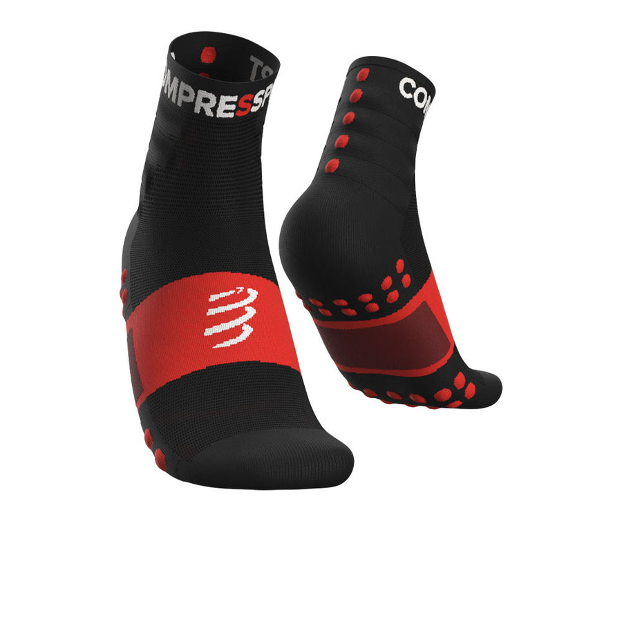 The Compressport Unisex Training Socks (2 Pack) feature black and red ankle-length designs with arch support, white logo, text, and red grip dots on soles and back. Breathable socks are shown from front and back on a white background.